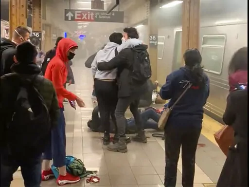 This photo provided by Will B Wylde,  a person is aided outside a subway car in the Brooklyn borough of New York, Tuesday, April 12, 2022. A gunman filled a rush-hour subway train with smoke and shot multiple people Tuesday, leaving wounded commuters bleeding on a Brooklyn platform as others ran screaming, authorities said. Police were still searching for the suspect. (Will B Wylde via AP)